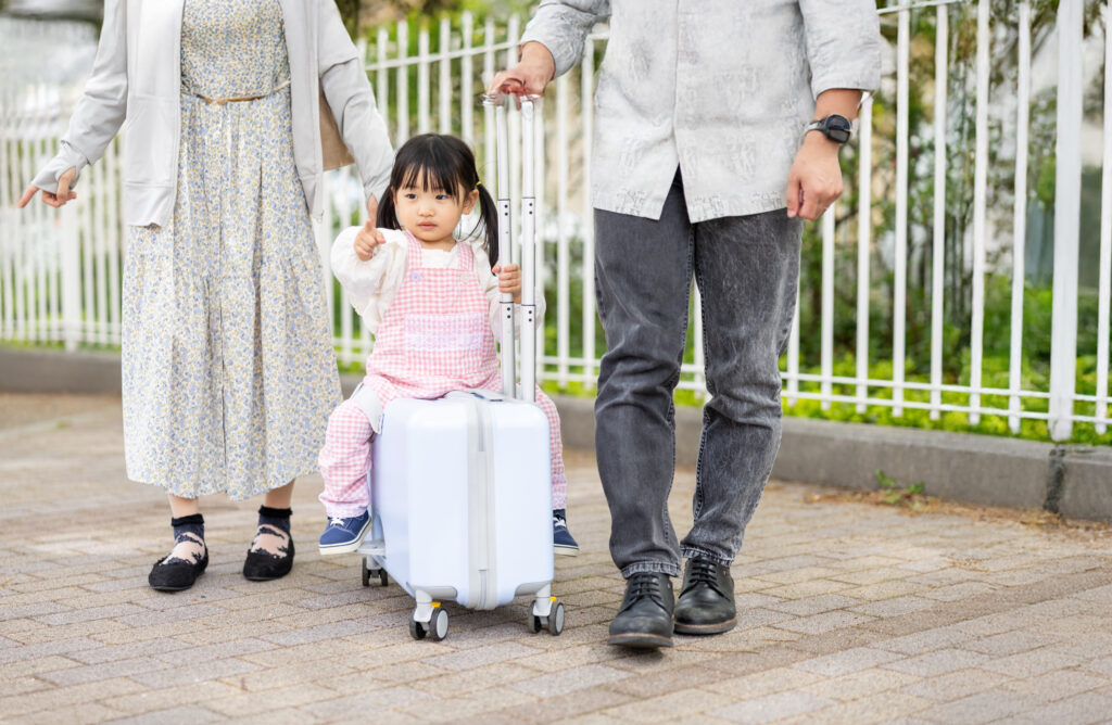 両親に囲まれてキャリーケースで移動する子ども