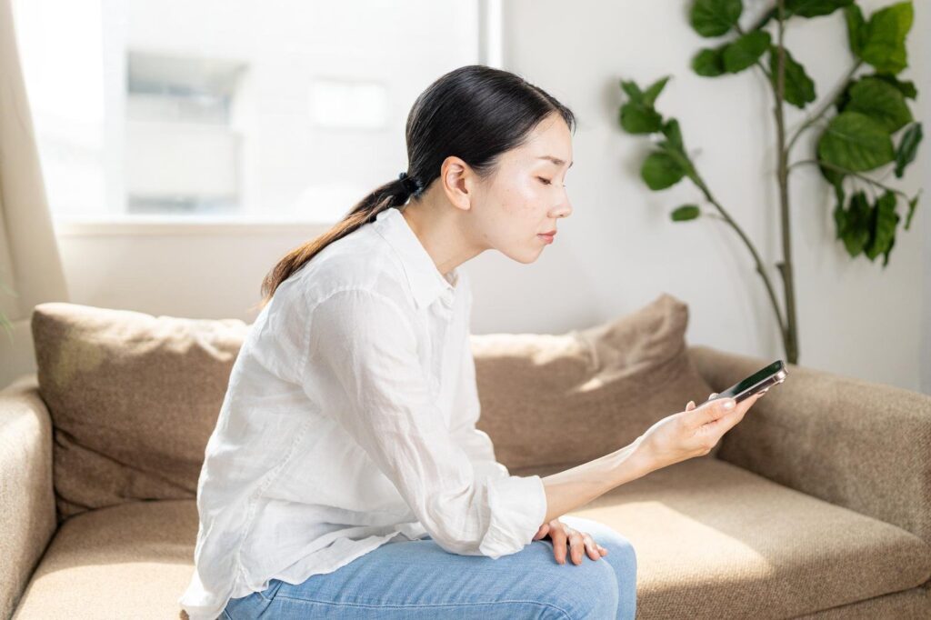 リビングのソファに座り、スマートフォンの画面を見る女性