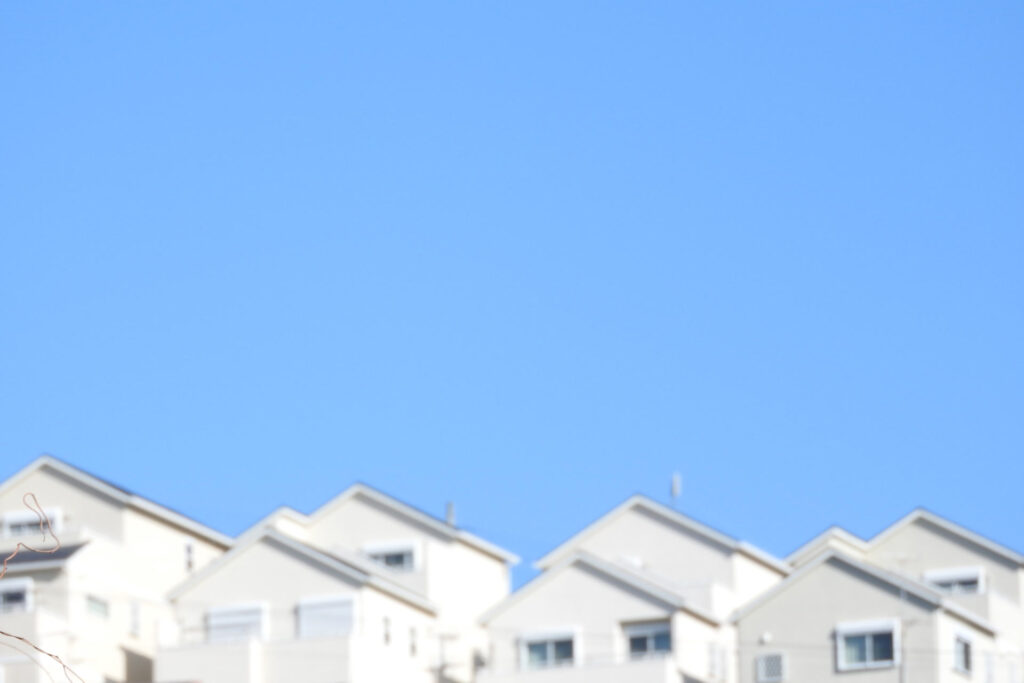 青空の下、丘の上に白い外壁の一戸建て住宅が並ぶ新しい住宅地