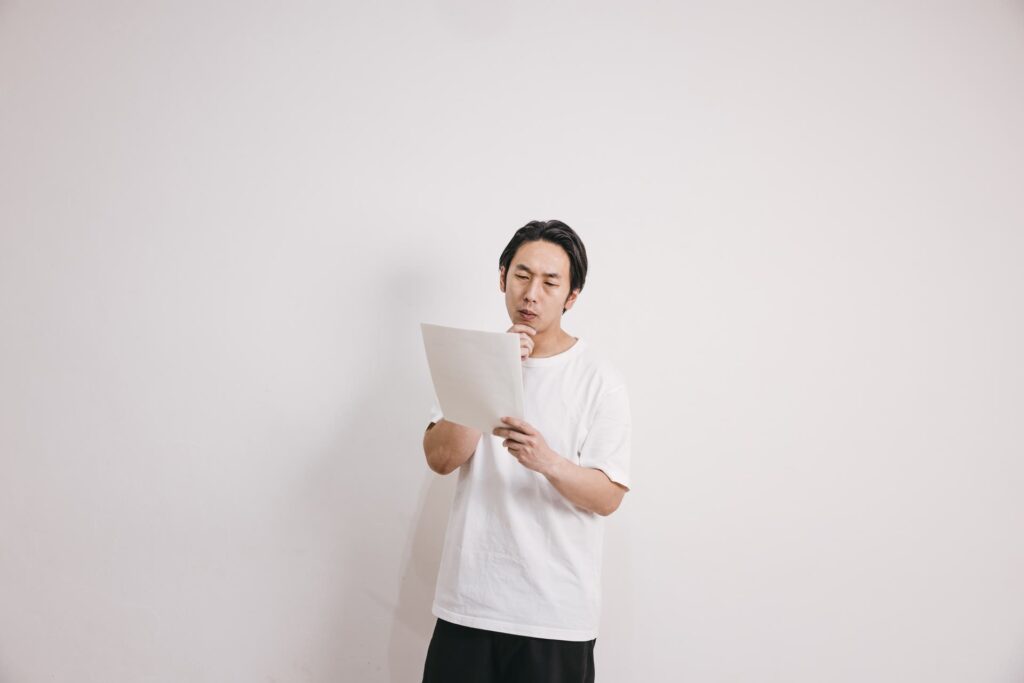 白い壁の前で健康診断の結果表を読む男性