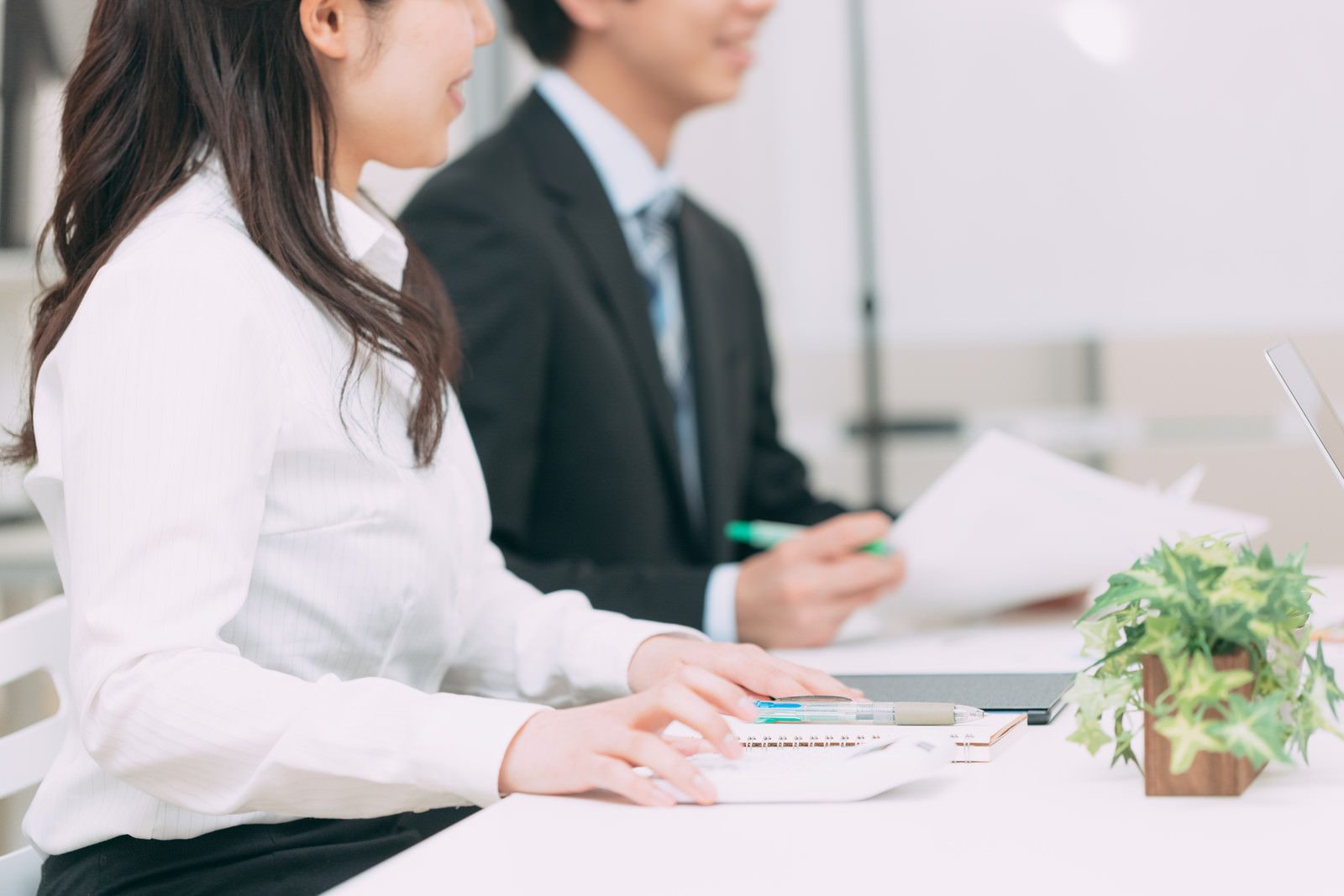 白いデスクで書類と電卓を前に打ち合わせをするスーツ姿の男女