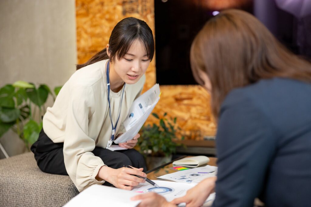 ソファ席で資料を広げ、ペンを手に内容を確認しながら話し合う二人の女性