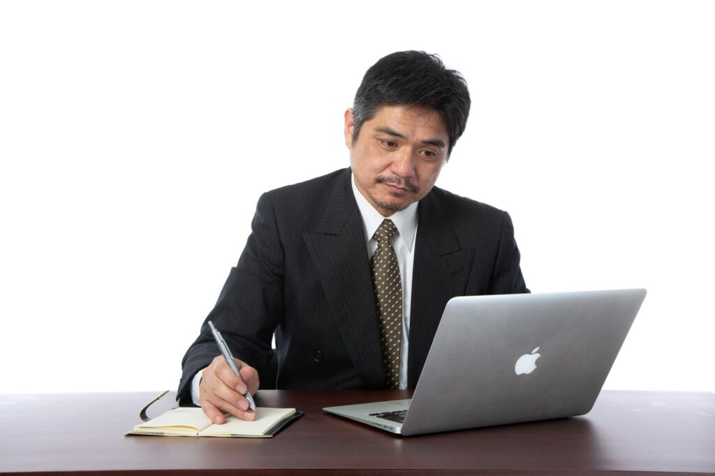 ノートPCを見ながらメモを取るスーツ姿の男性