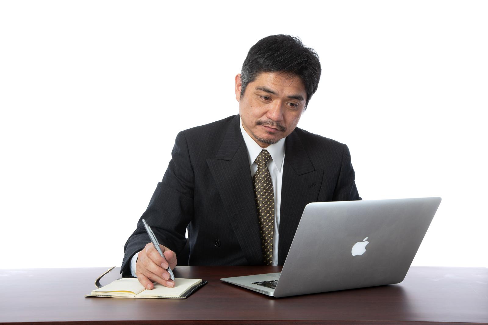 ノートPCを見ながらメモを取るスーツ姿の男性